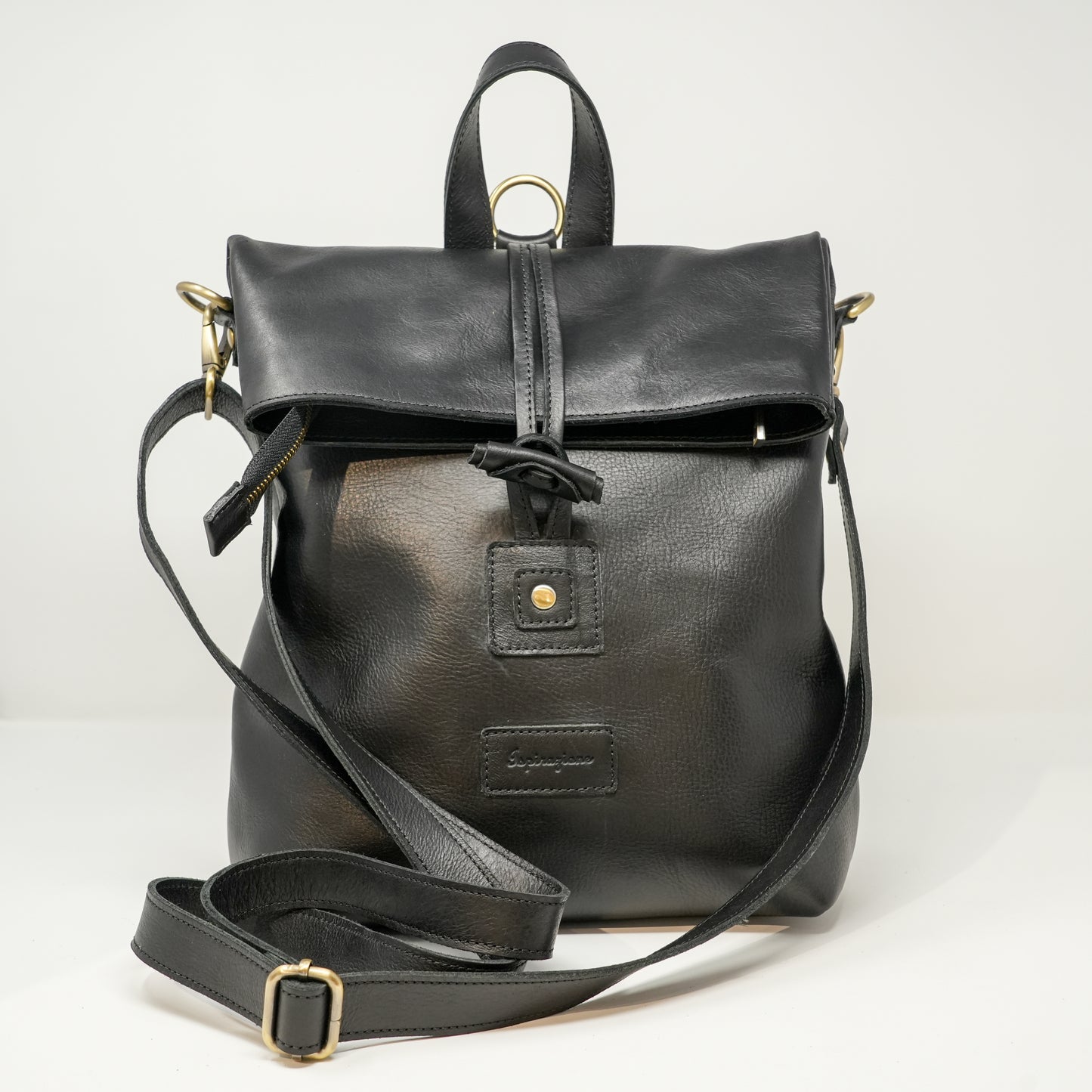 Borsa zaino in pelle nera con chiusura a laccio e  cerniera , manico superiore e tracolla regolabile. Accessori metallici dorati e dettaglio con bottone anteriore.